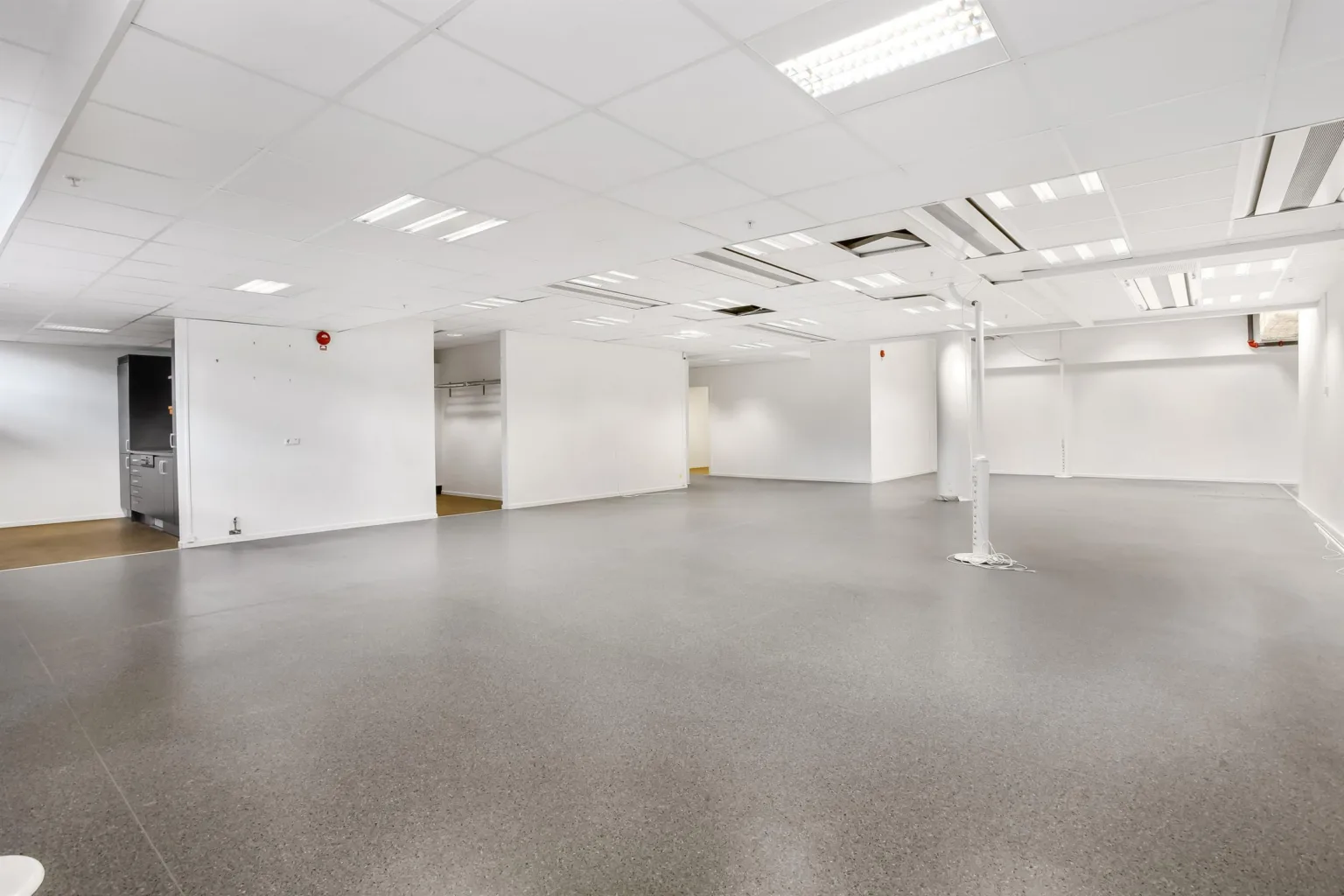 Rymlig lokal med vita väggar, grå golv och tak med ventilationssystem.