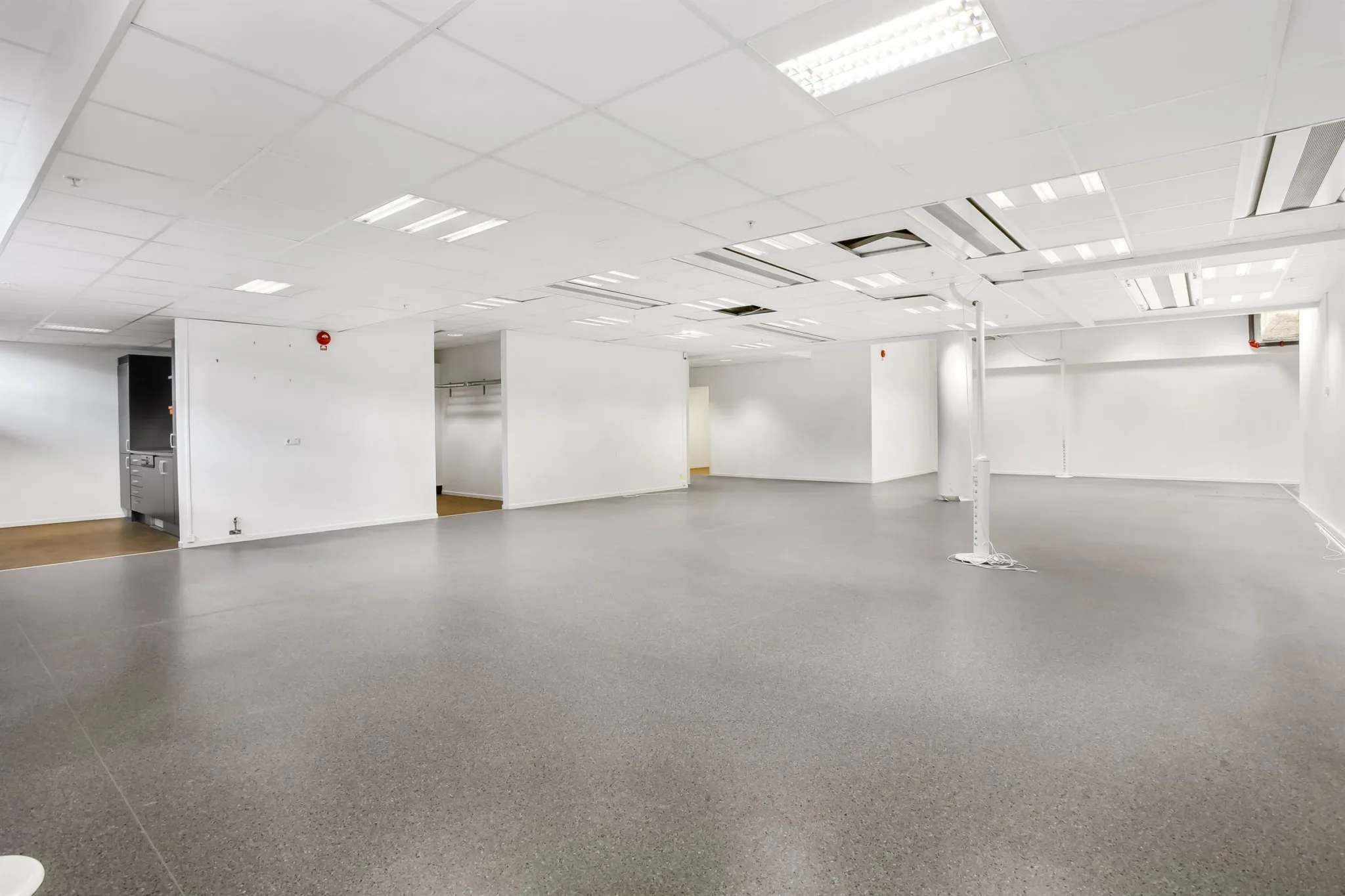 Rymlig lokal med vita väggar, grå golv och tak med ventilationssystem.
