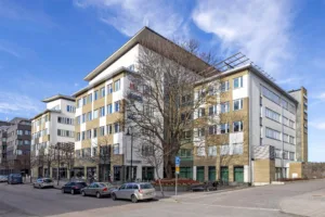 En modern byggnad med flera våningar, vita fasader och träd framför.