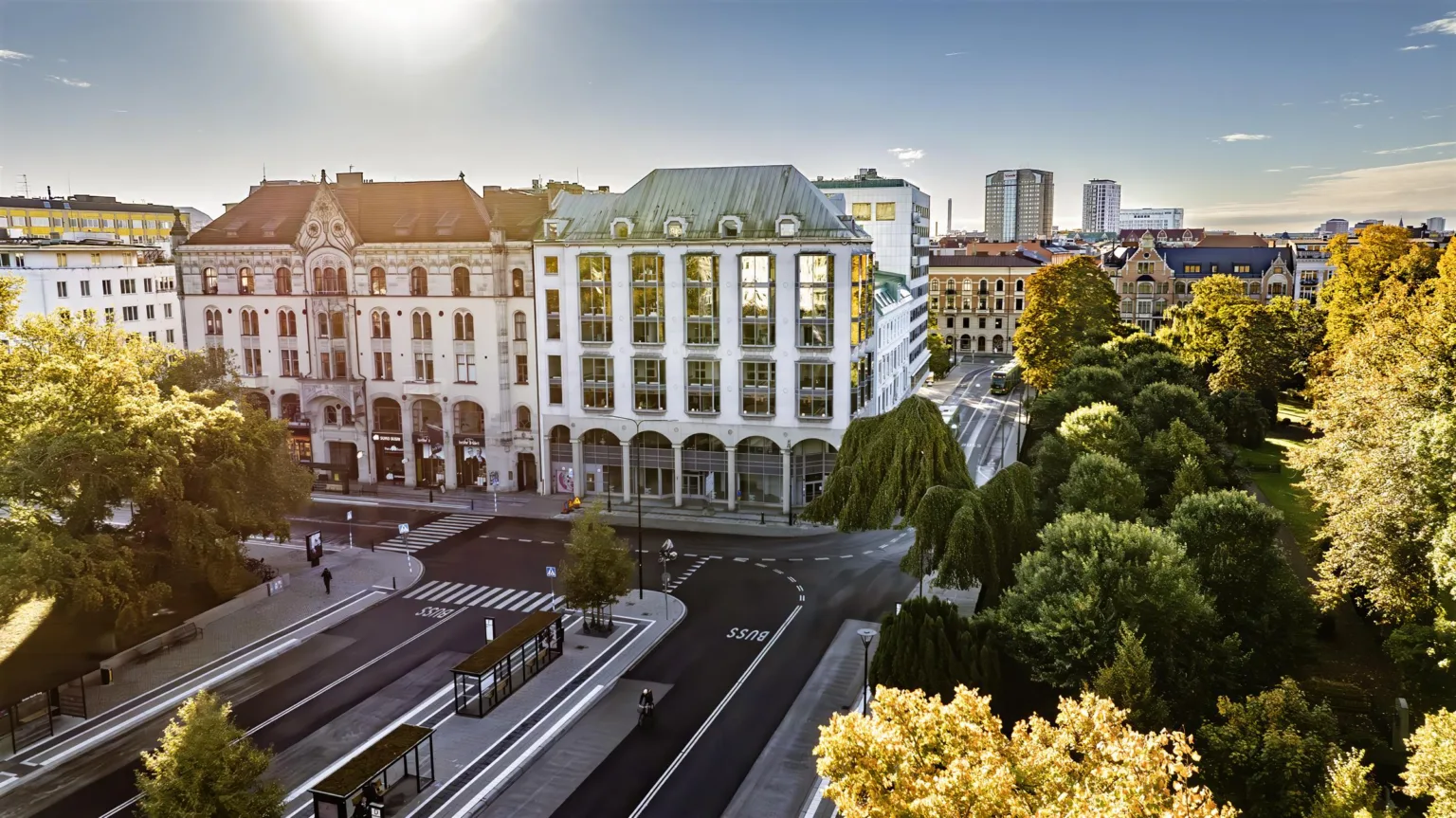En stadsbild med historiska och moderna byggnader, soligt väder och grönska.