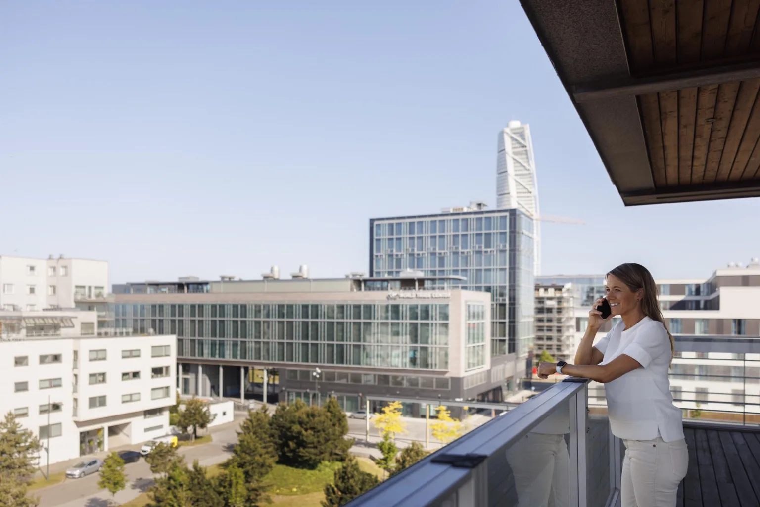 En kvinna står på en balkong och tittar ut över ett stadslandskap med moderna byggnader och Turning Torso i bakgrunden.