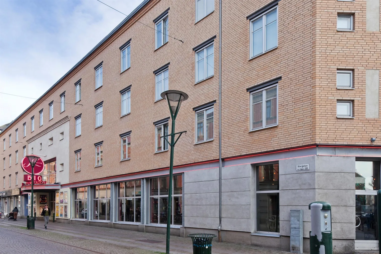 En flerbostadsbyggnad med beige fasad och stora fönster på bottenvåningen längs en gata.