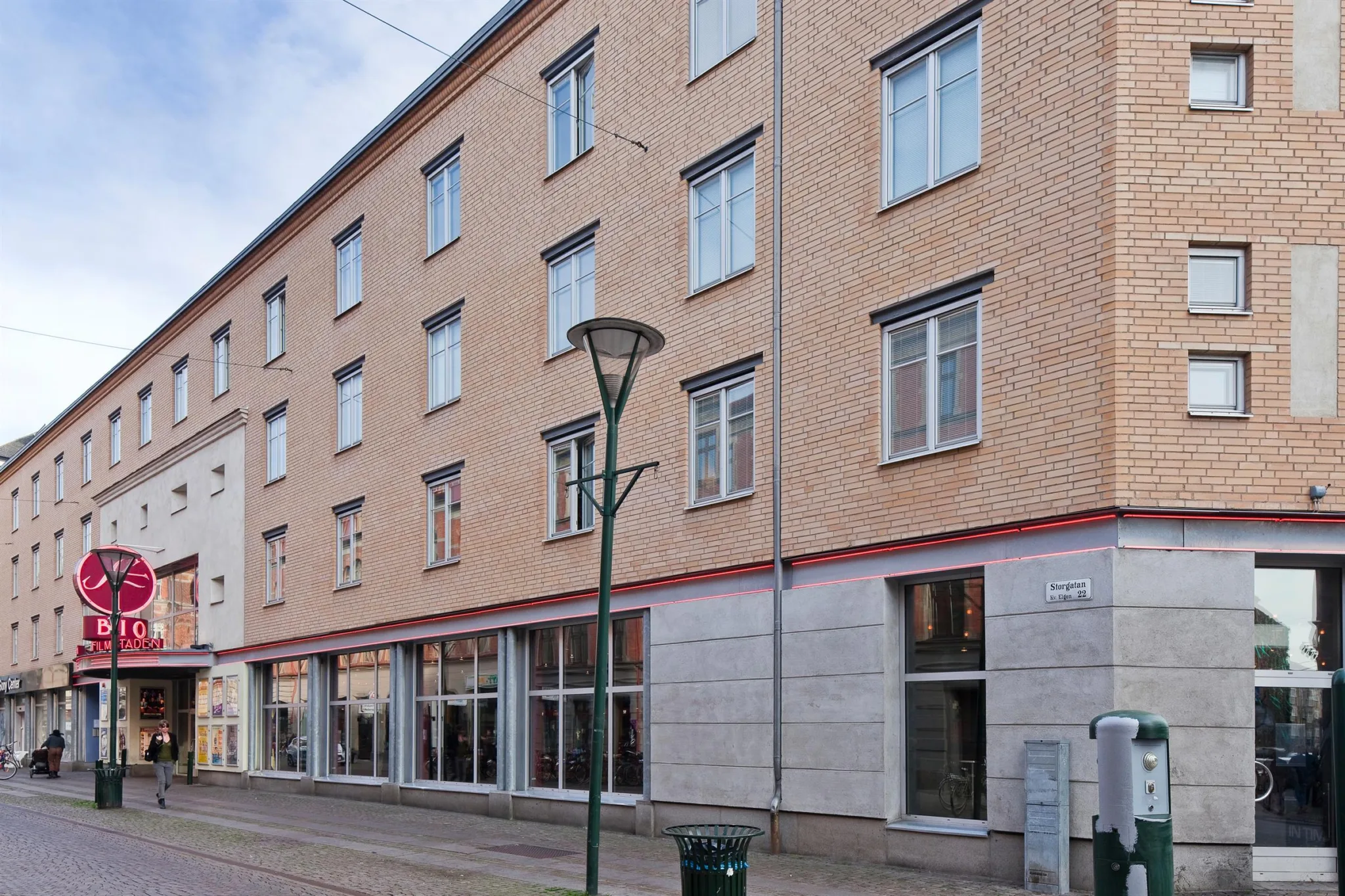 En flerbostadsbyggnad med beige fasad och stora fönster på bottenvåningen längs en gata.