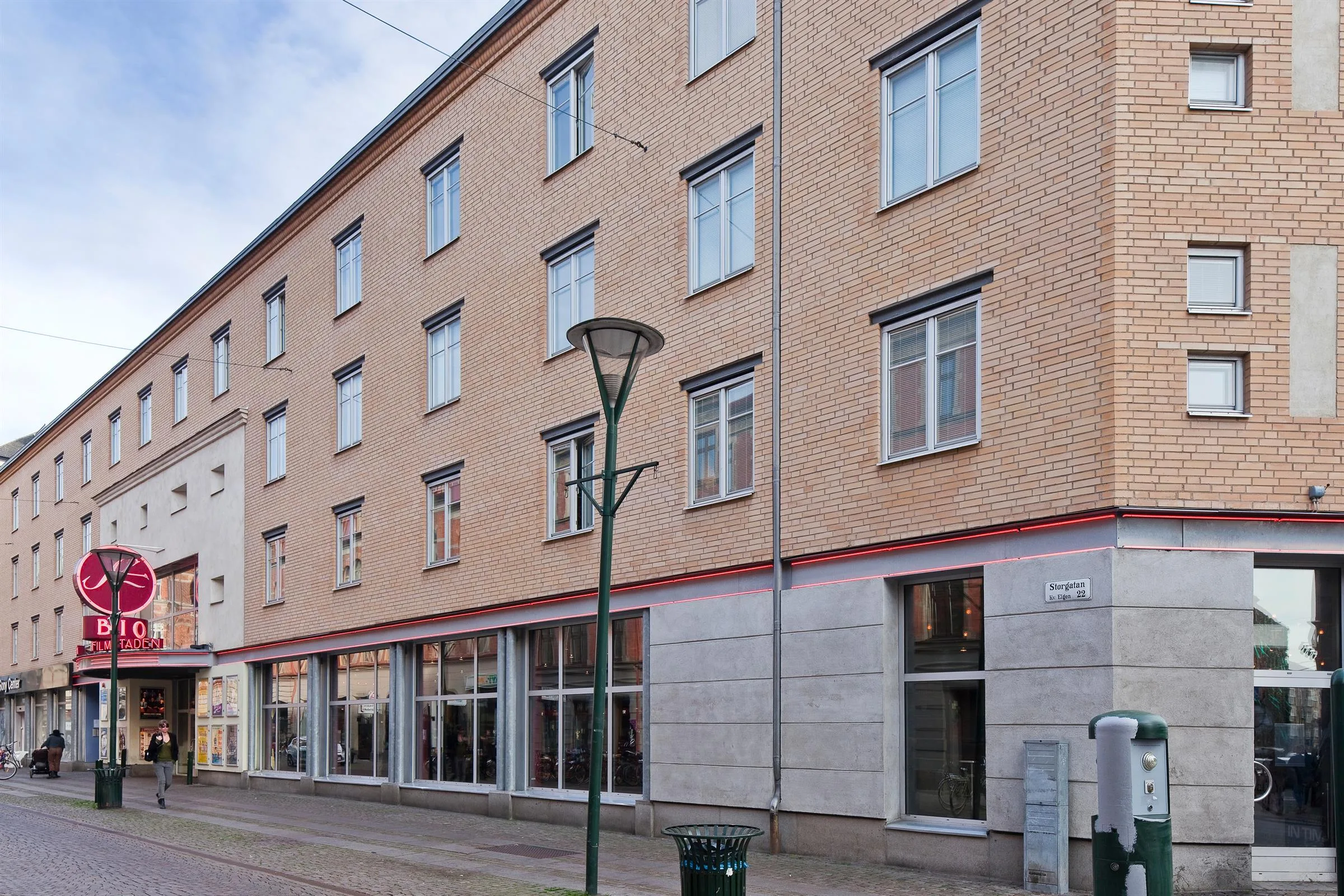 En flerbostadsbyggnad med beige fasad och stora fönster på bottenvåningen längs en gata.