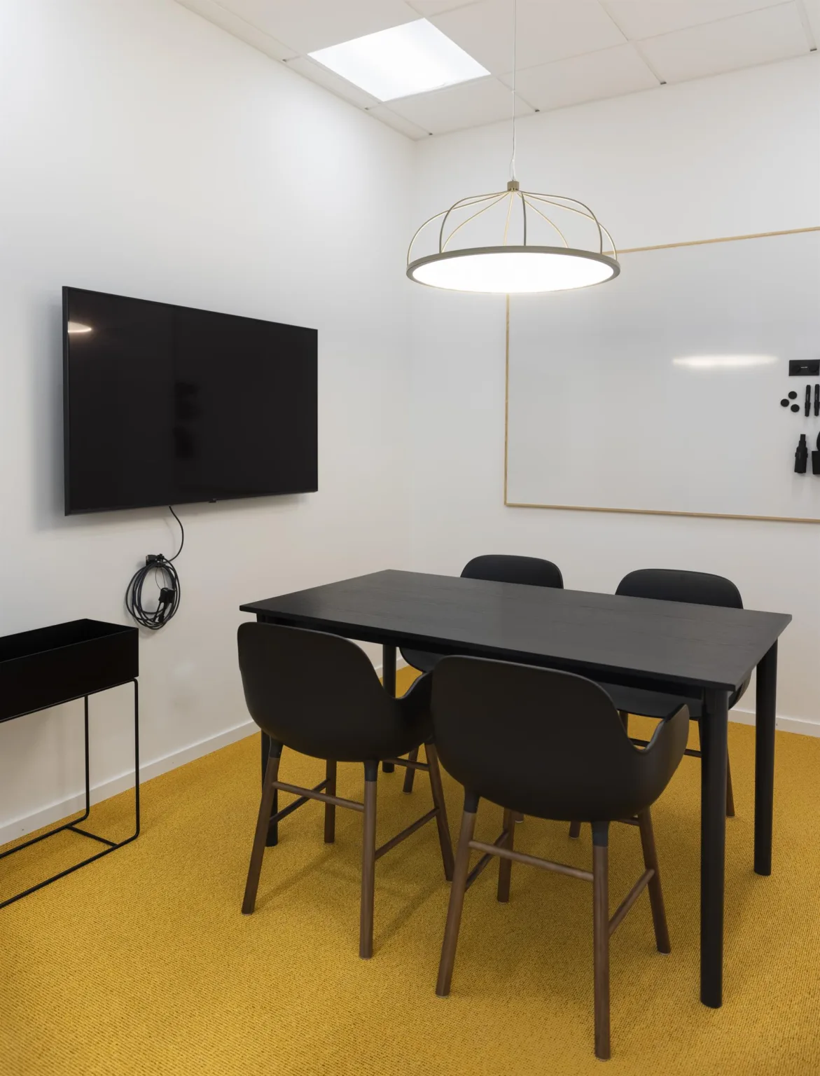 5. Ett mötesrum med ett svart bord, fyra svarta stolar, en väggmonterad TV och en whiteboard.