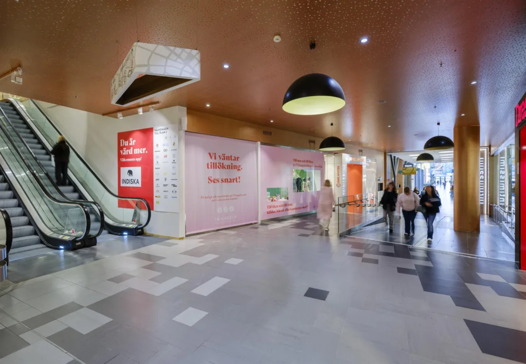 2. En köpcentrumgång med rosa väggar, röda reklamskyltar och några personer som går förbi.