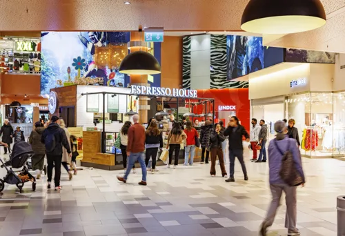 En livlig shoppinggalleria med människor som går förbi olika butiker och serveringar.