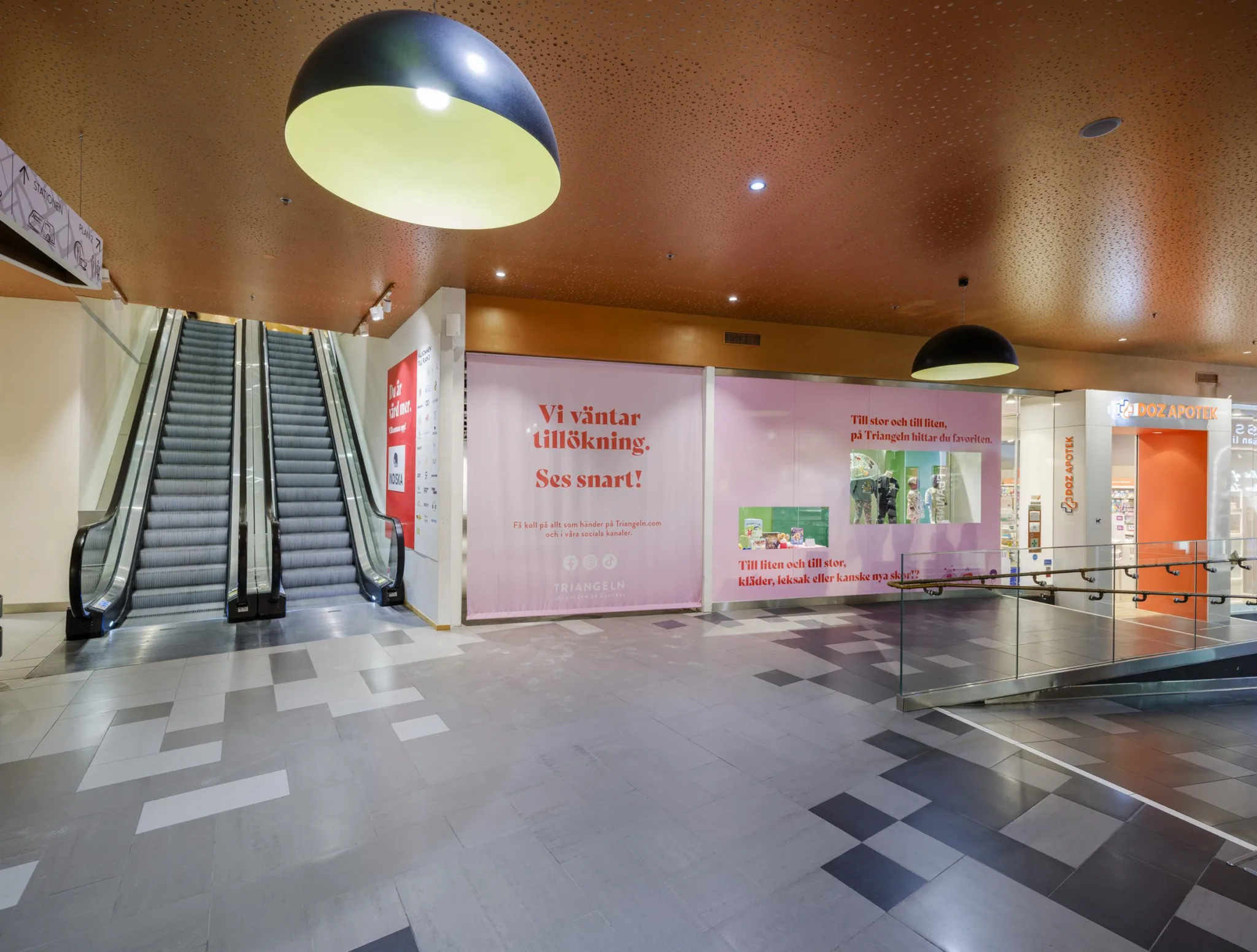 3. En köpcentrumgång med rosa väggar, rulltrappor till vänster och stora taklampor.