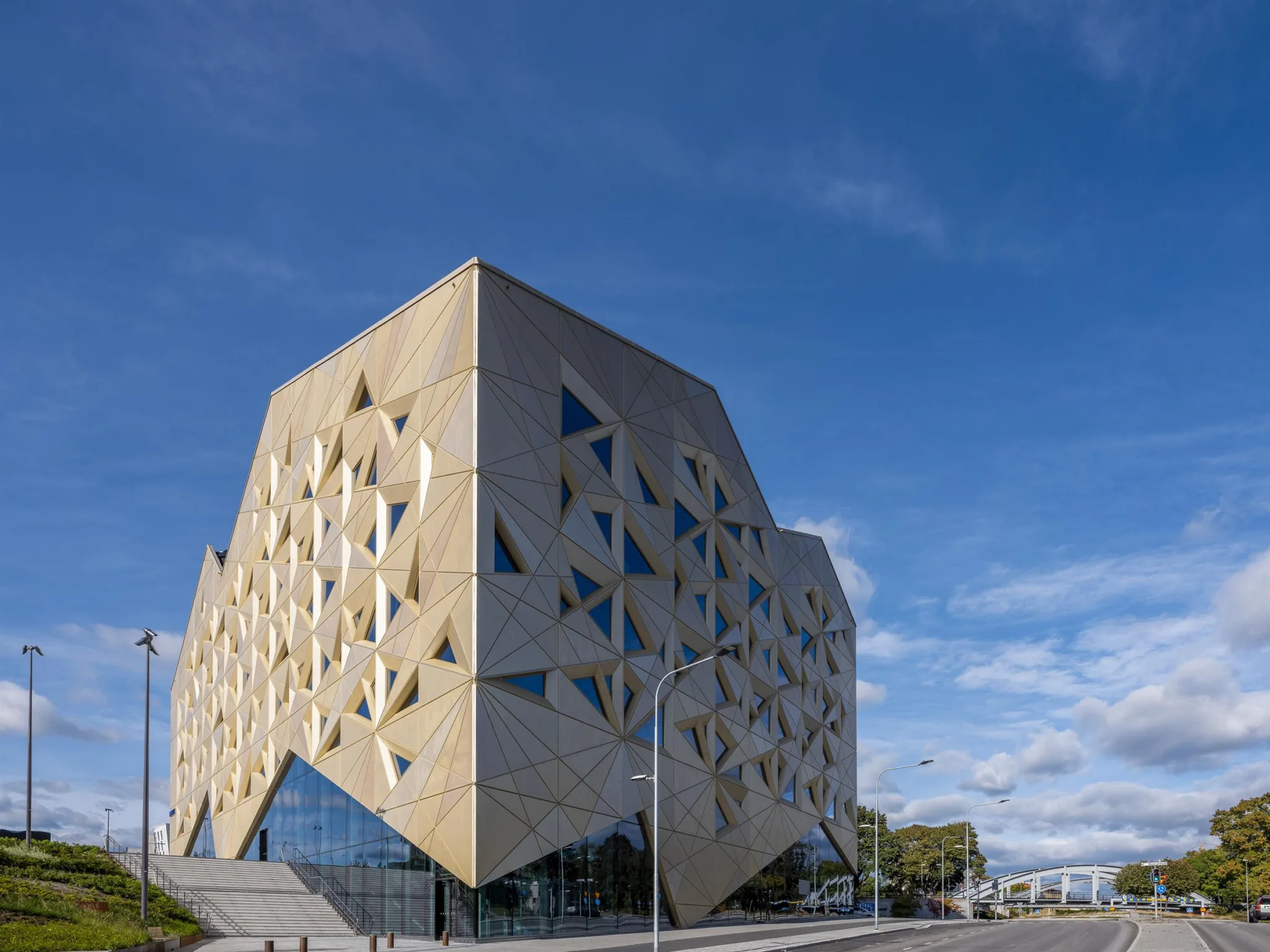 En arkitektonisk byggnad med unik geometrisk design, belägen under en blå himmel med moln.