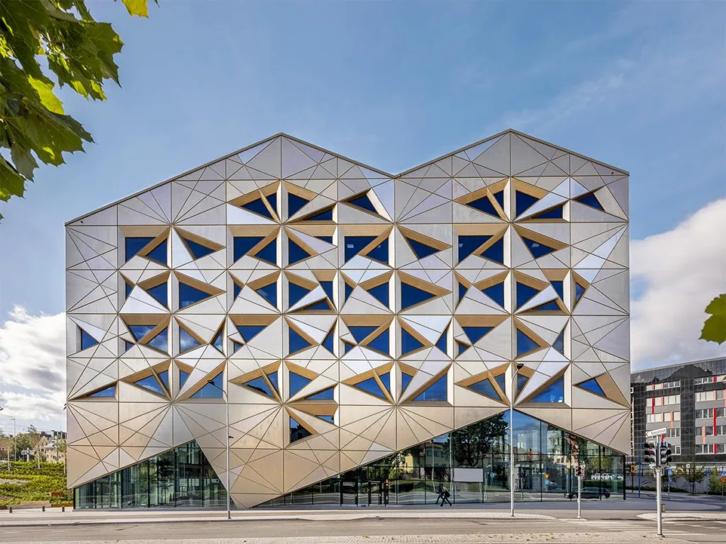 2. En modern byggnad med en geometrisk fasad av triangulära fönster och paneler under en klar himmel.