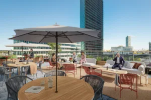 Takterrass med bord, stolar, parasoll och människor som umgås med stadsutsikt i bakgrunden.