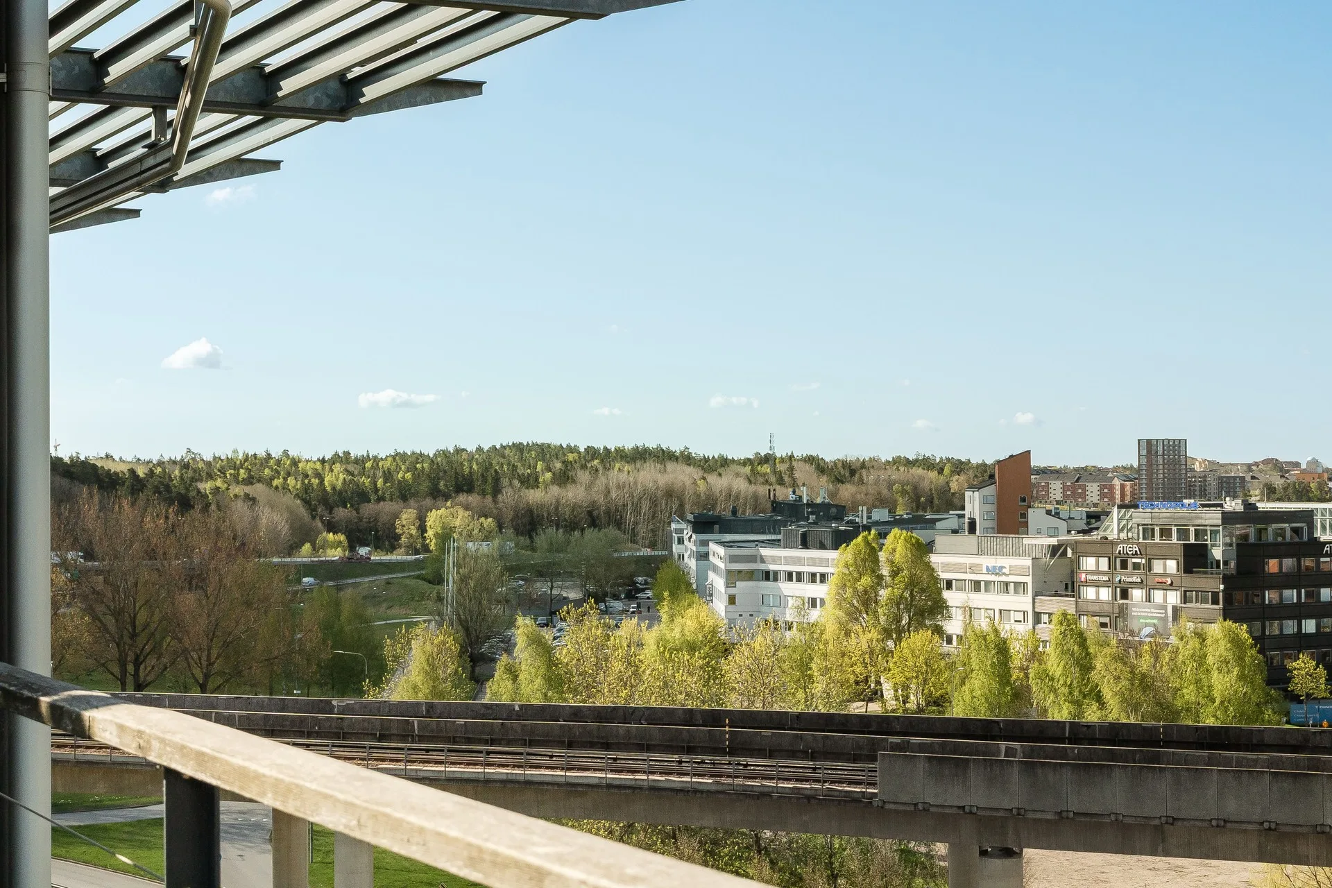 Vy över en byggnad omgiven av grönska och skog under en klarblå himmel.