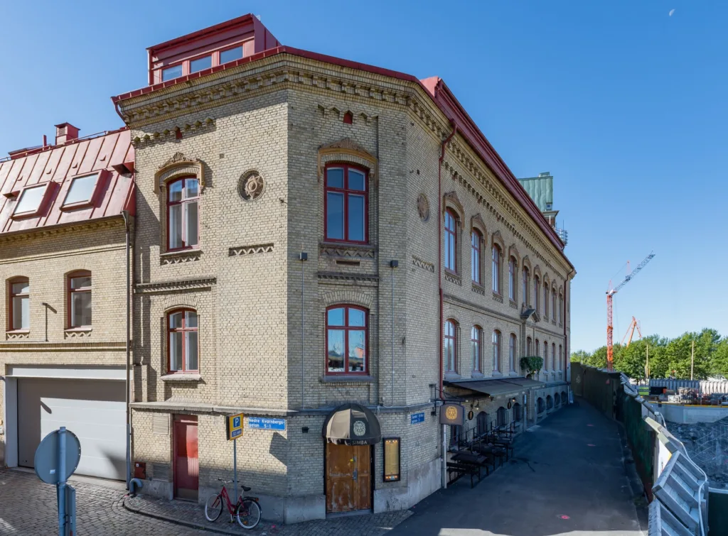 En äldre byggnad i gul tegel med röda tak och fönster, cyklar står parkerade vid fasaden.