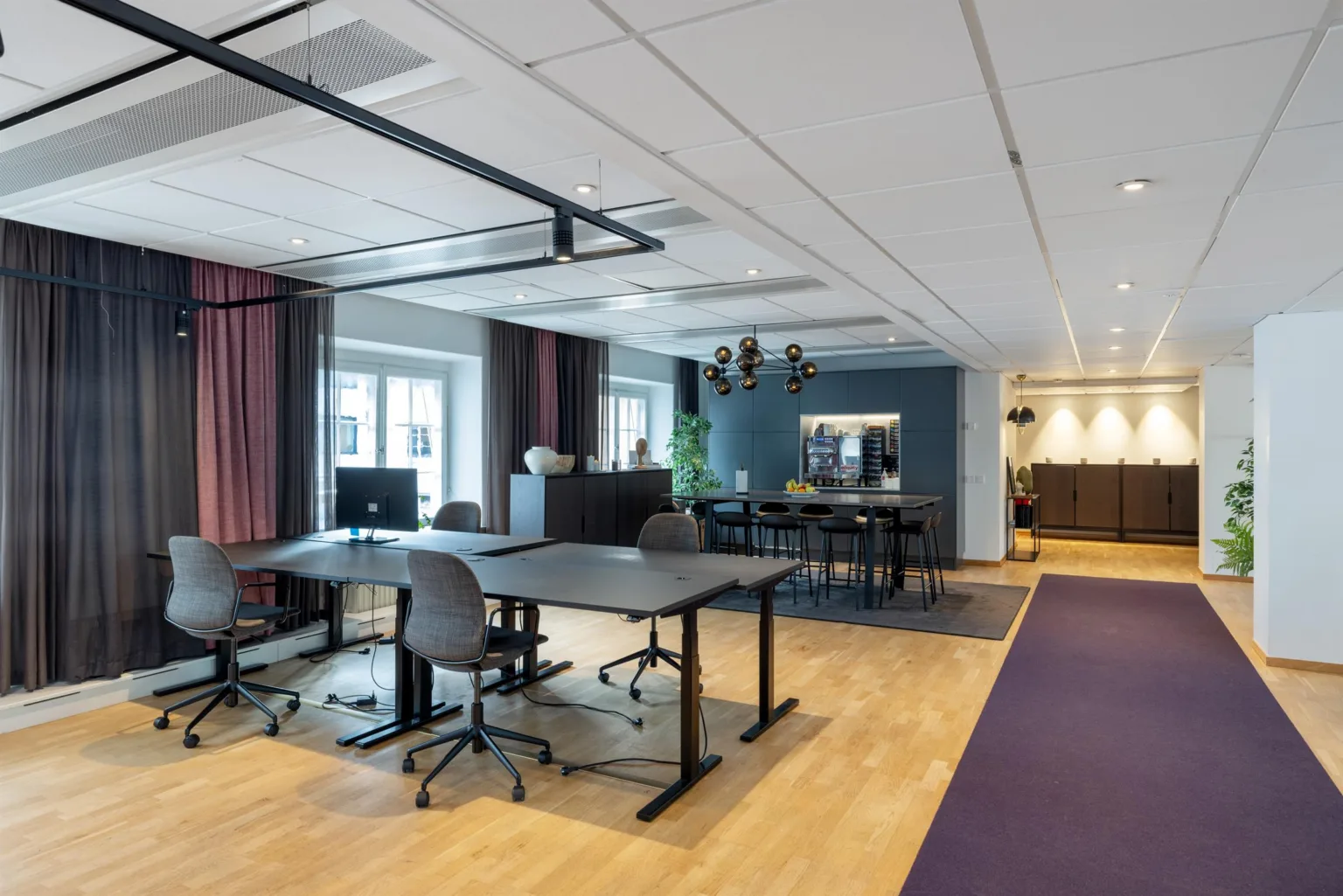 Ett öppet kontorsutrymme med skrivbord, kontorsstolar, växter och en loungeområde i bakgrunden.