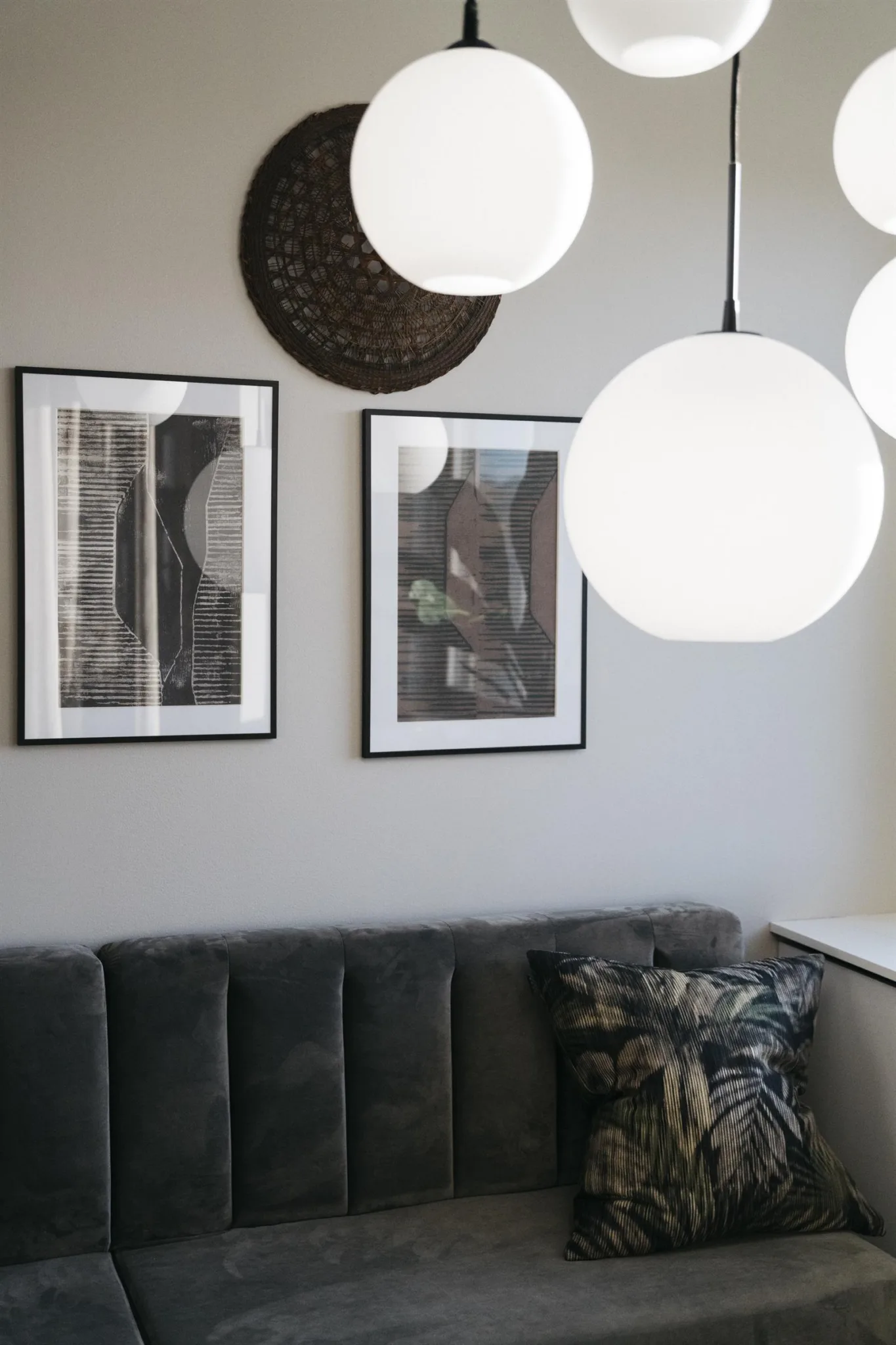 En grå soffa med prydnadskuddar under tre inramade tavlor och runda vita lampor hängande från taket.