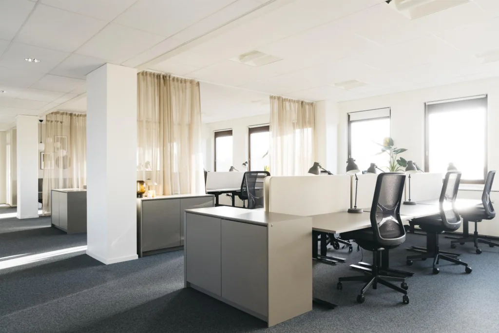 En kontorsmiljö med arbetsstationer, stolar och gardiner som delar upp utrymmet.