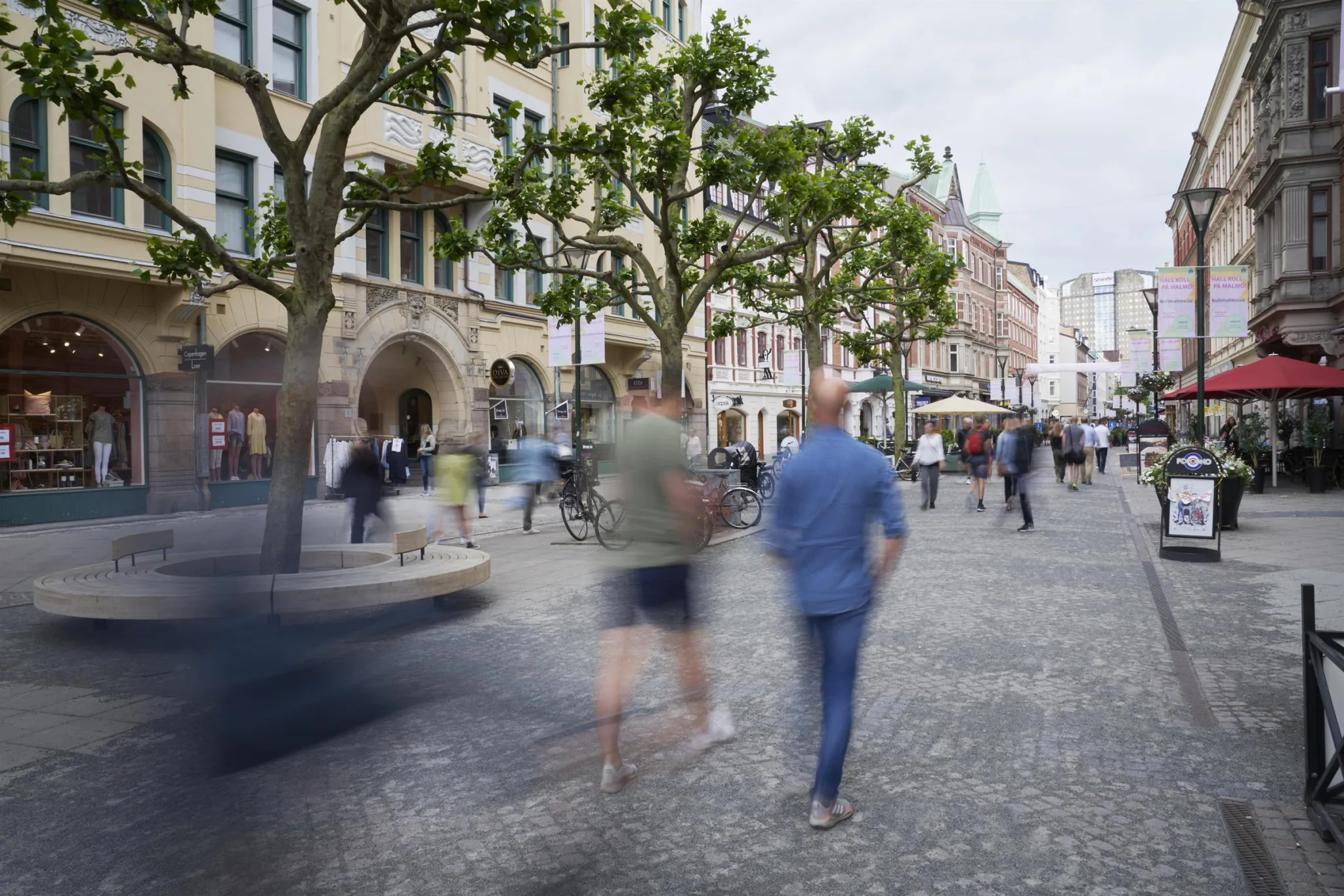 1. En stadsgata med människor som promenerar förbi träd och byggnader.