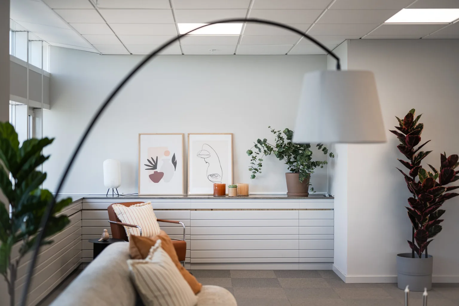 2. Vardagsrum med soffa, kuddar, en bågformad lampa och tavlor på en hylla.