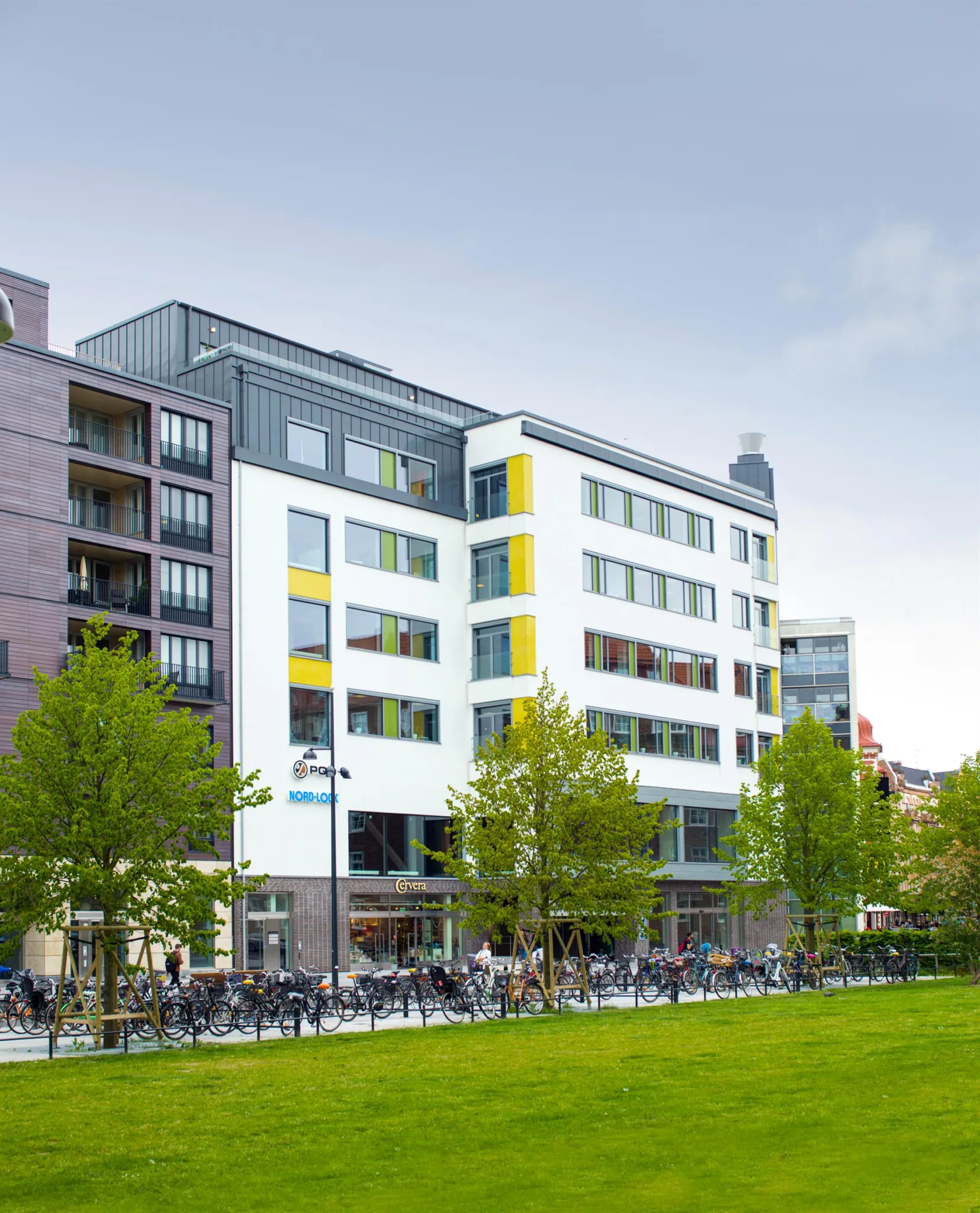 En modern byggnad med vit fasad och färgglada detaljer, omgiven av gröna träd och en gräsmatta.