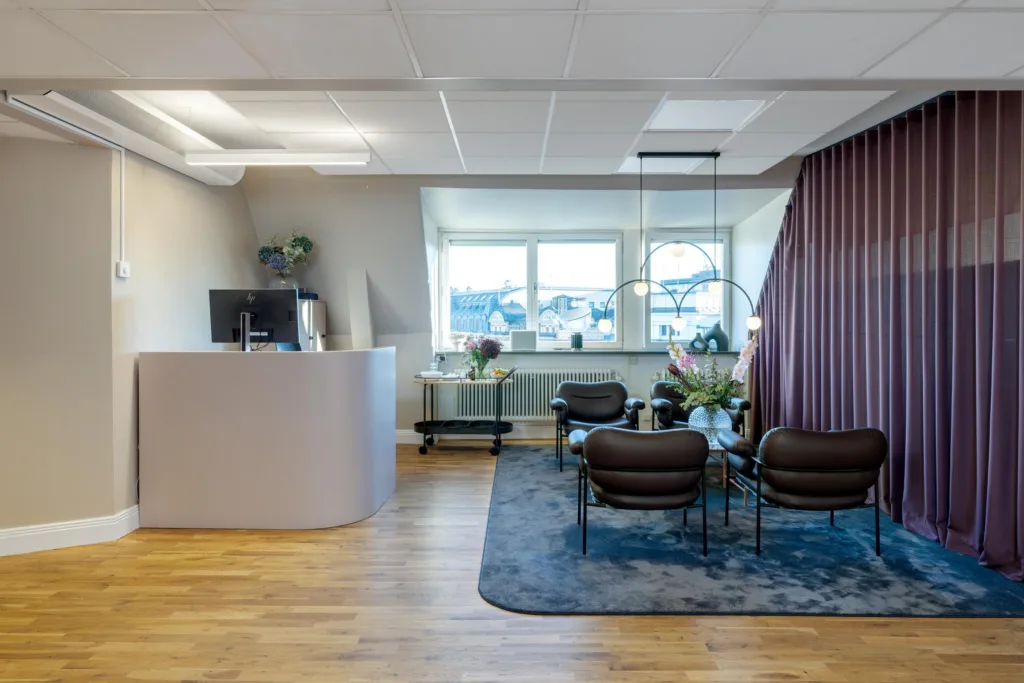 Ett modernt väntrum med reception, sittgrupp och stora fönster som släpper in ljus.