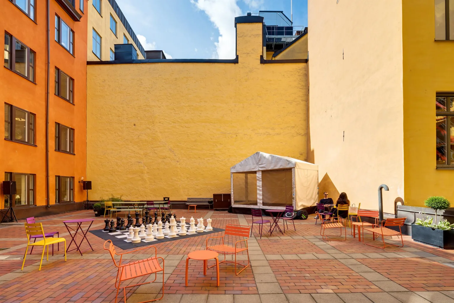 En utomhusterrass med stora väggar, schackbräde, orangea utemöbler och ett tält.
