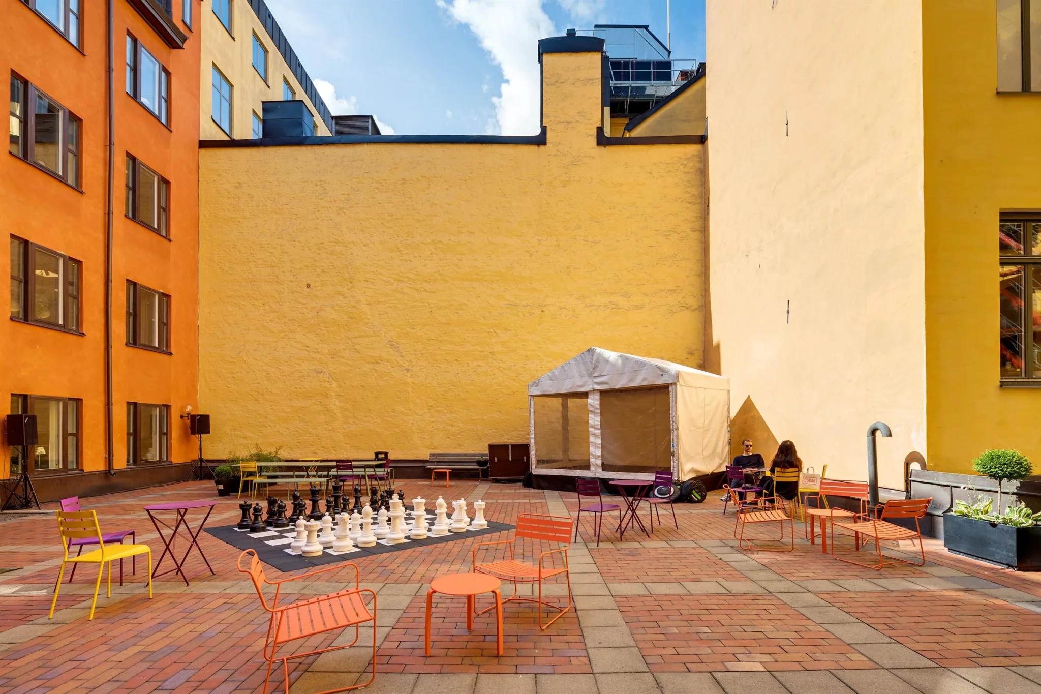 En utomhusterrass med stora väggar, schackbräde, orangea utemöbler och ett tält.