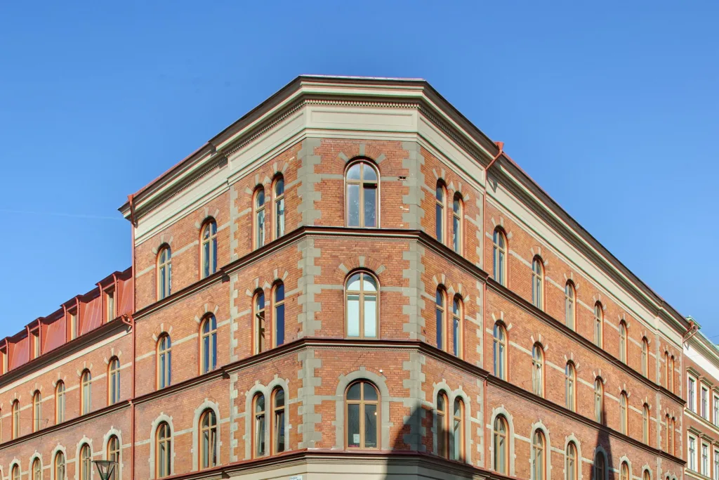 Hörn av en tegelbyggnad med många bågformade fönster och detaljerade fasader under klar himmel.