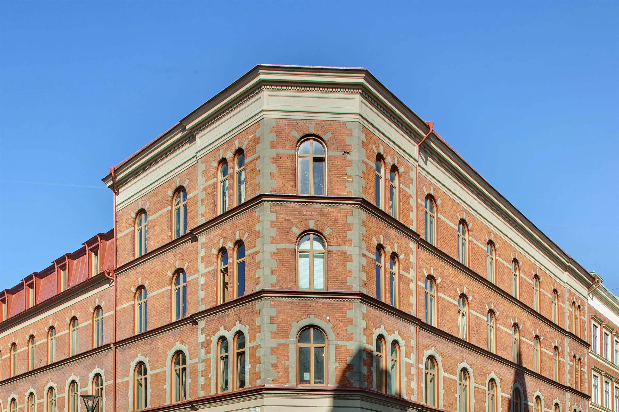 Hörn av en tegelbyggnad med många bågformade fönster och detaljerade fasader under klar himmel.