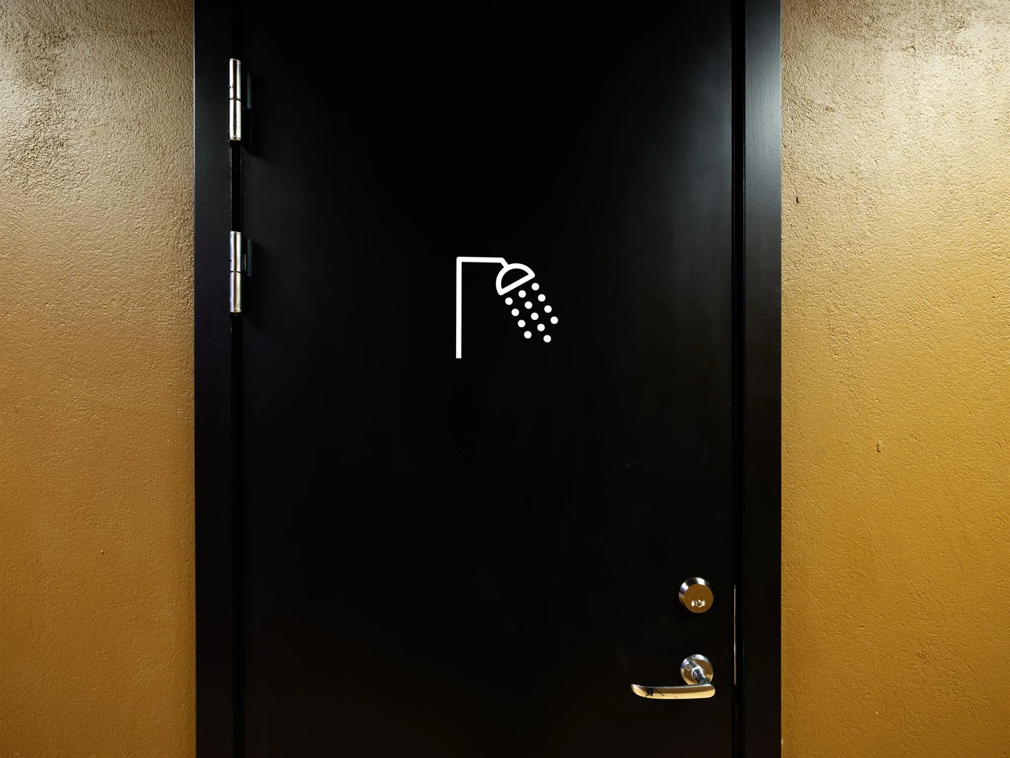 En svart dörr med en vit symbol av en dusch på, omgiven av en orange vägg.