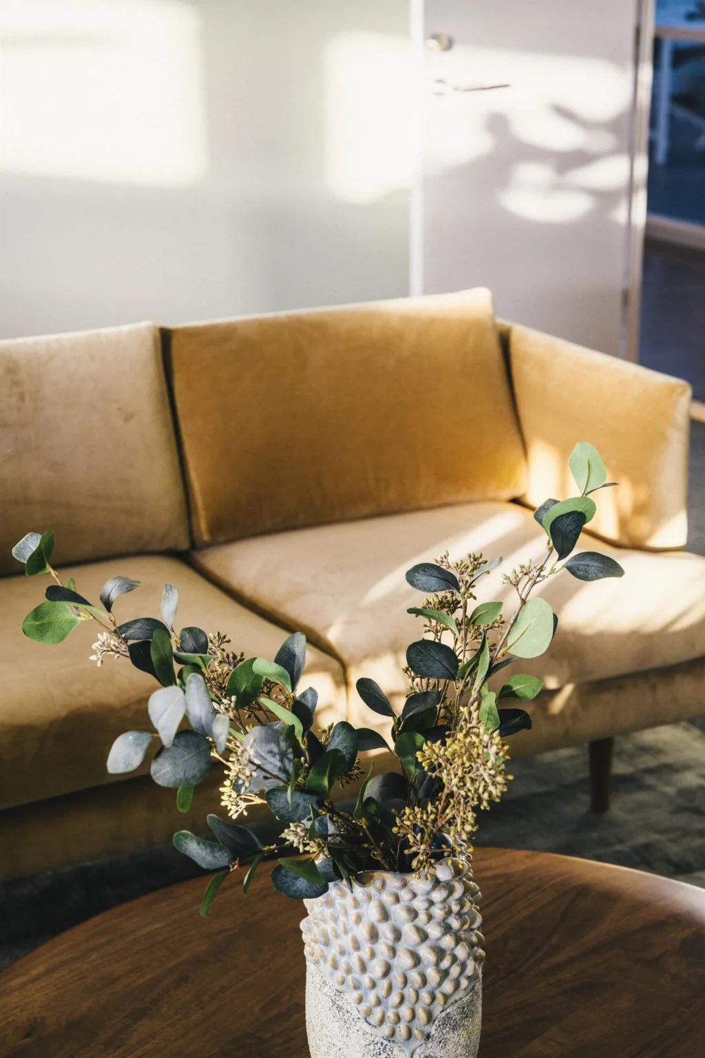 5. En närbild av en gul sammetssoffa med en vas fylld med gröna kvistar och blommor på ett bord framför.