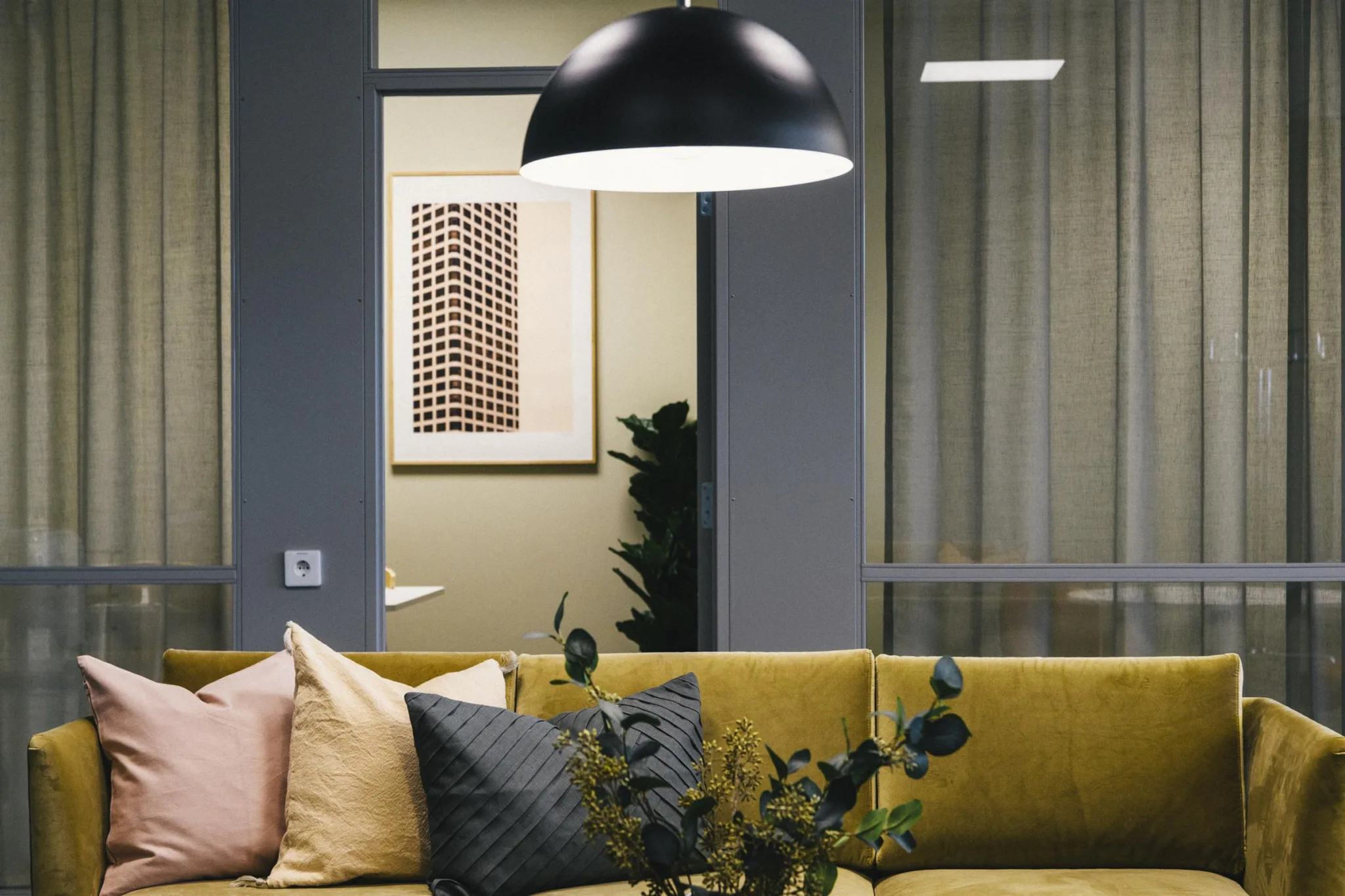 4. En gul soffa med färgglada kuddar under en stor svart taklampa, med en tavla och växter i bakgrunden.