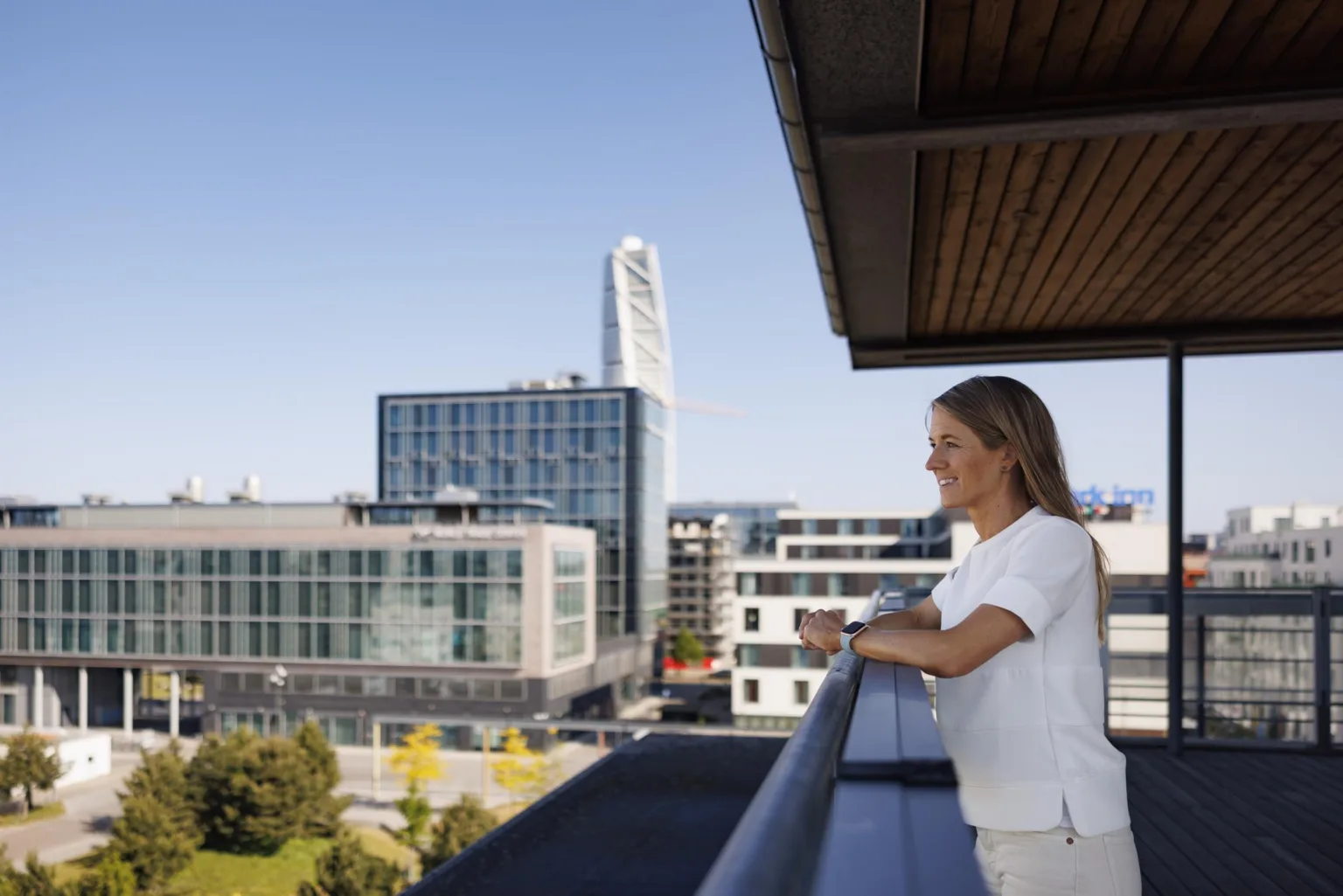 En kvinna står på en balkong och tittar ut över en stad med moderna byggnader, inklusive Turning Torso i bakgrunden.