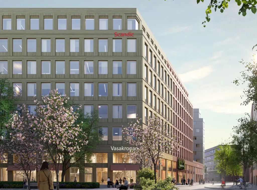 Grön byggnad med stora glasfönster och vårblommande träd framför.