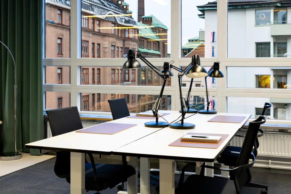 5. Ett kontor med skrivbord, svarta stolar och skrivbordslampor, stora fönster visar byggnader utanför.