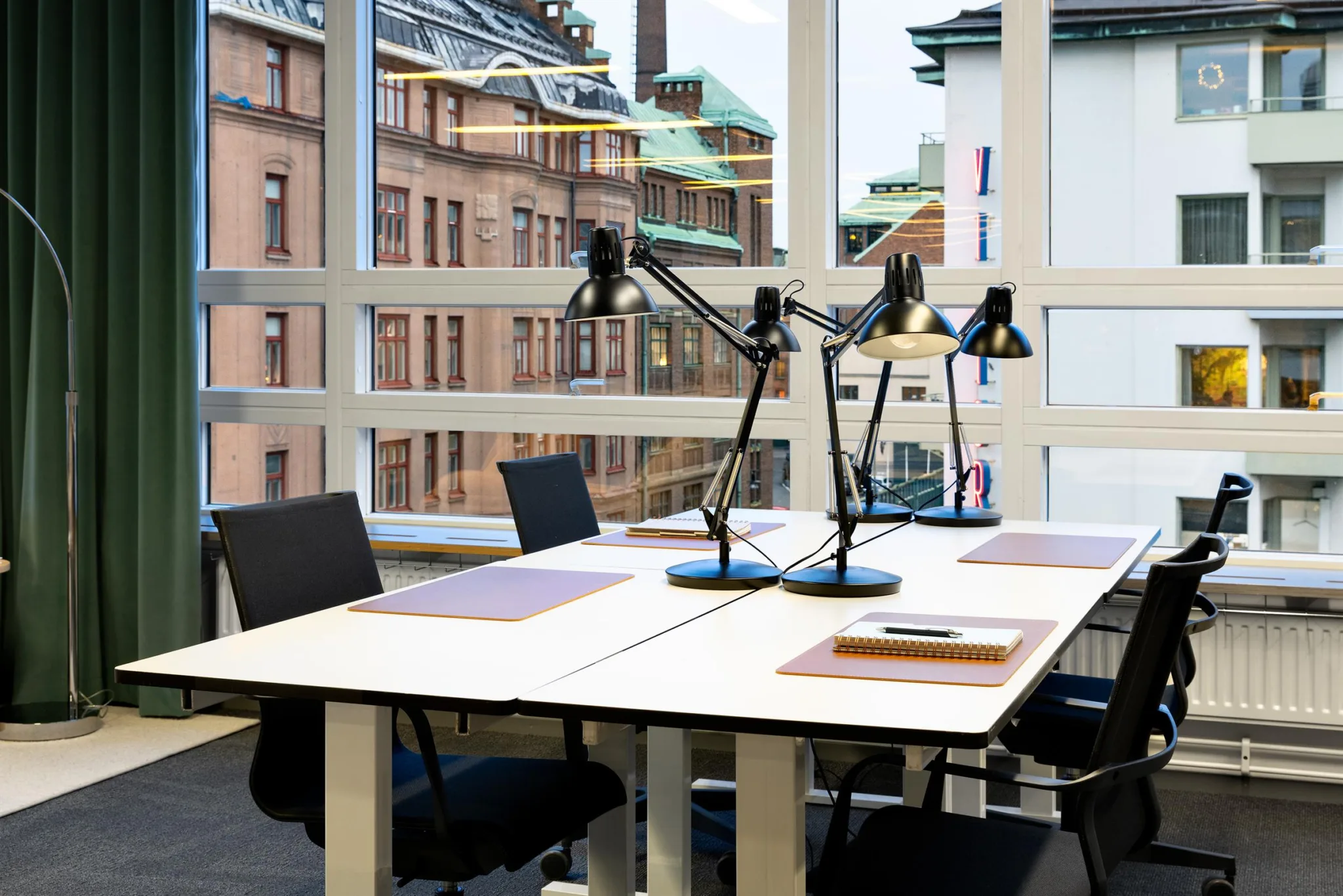 5. Ett kontor med skrivbord, svarta stolar och skrivbordslampor, stora fönster visar byggnader utanför.
