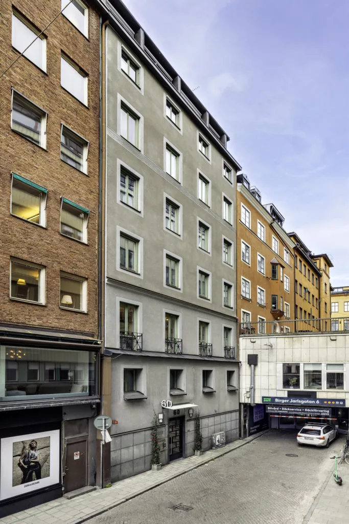 En smal gata med flerbostadshus i olika färger och arkitektoniska stilar, tydliga fönster och skyltar på fasaderna.