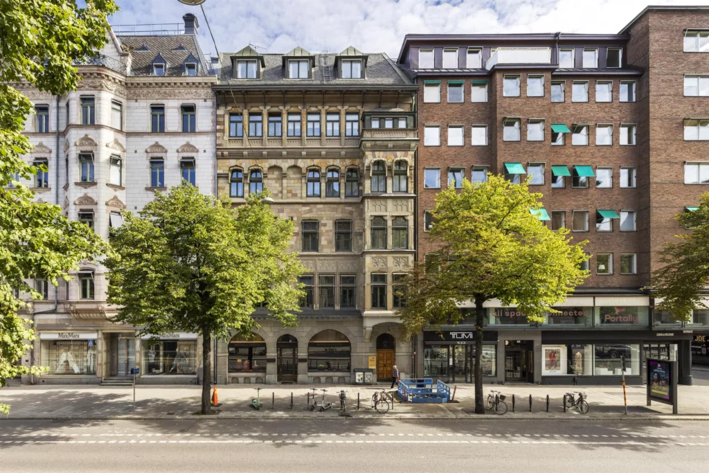 En rad av byggnader med olika arkitektoniska stilar, gröna träd längs gatan framför dem.
