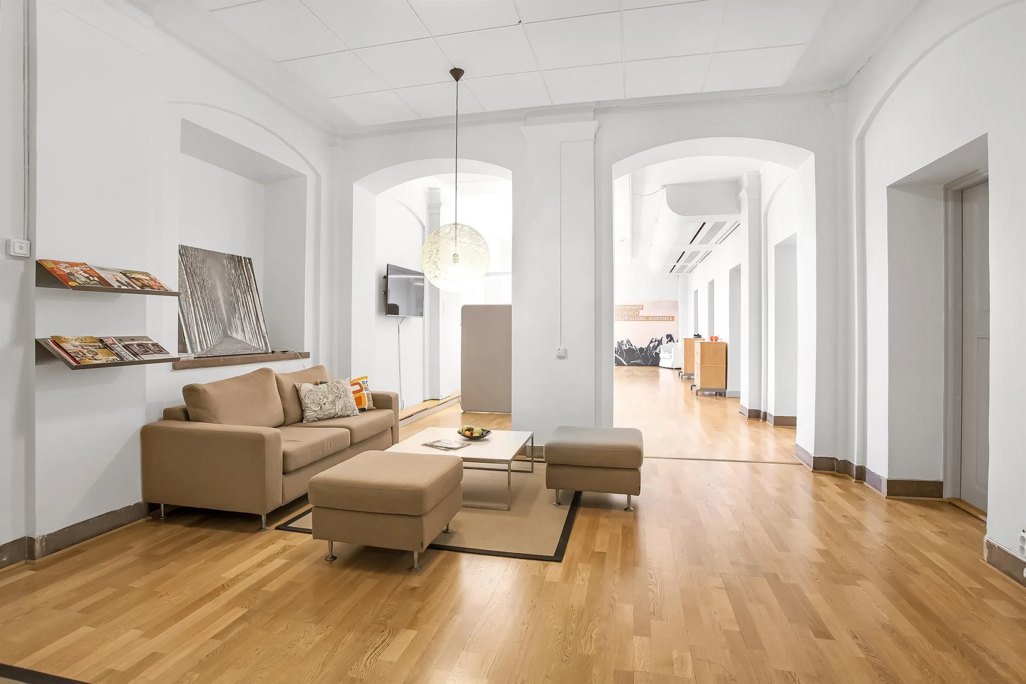 Ett ljust vardagsrum med beige soffa, soffbord och träparkettgolv. I bakgrunden syns en öppen planlösning med valvbågar.