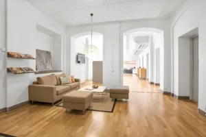 Ett ljust vardagsrum med beige soffa, soffbord och träparkettgolv. I bakgrunden syns en öppen planlösning med valvbågar.