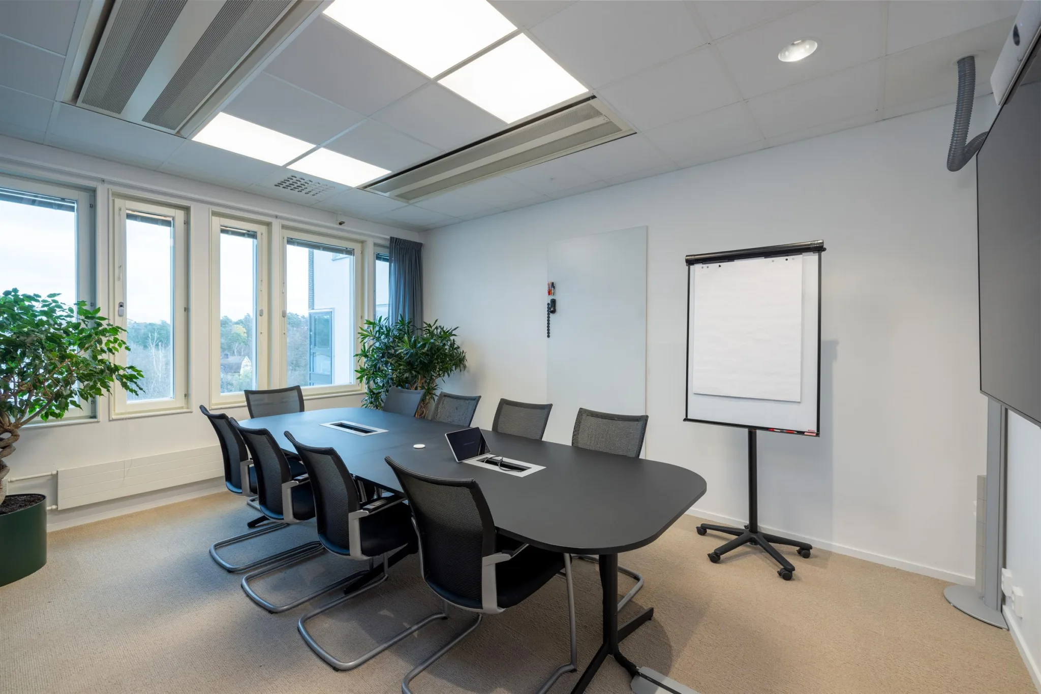 3. Ett konferensrum med ett ovalt bord, flera stolar, en whiteboard och ett fönster med utsikt.