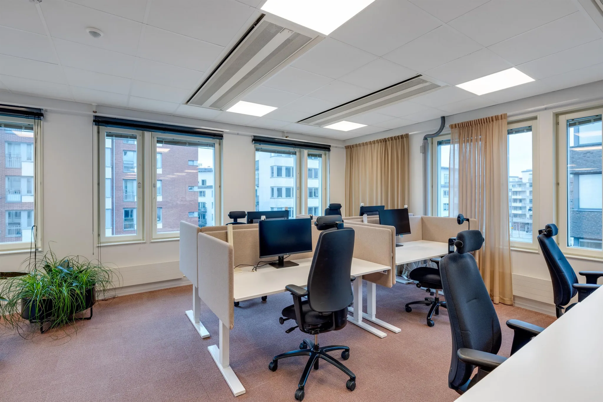 3. Arbetsstationer med svarta kontorsstolar och datorer, placerade framför stora fönster med stadsutsikt.