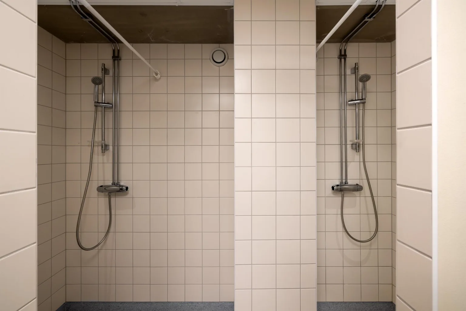 Två duschar med kaklade väggar, separerade av en kaklad pelare.