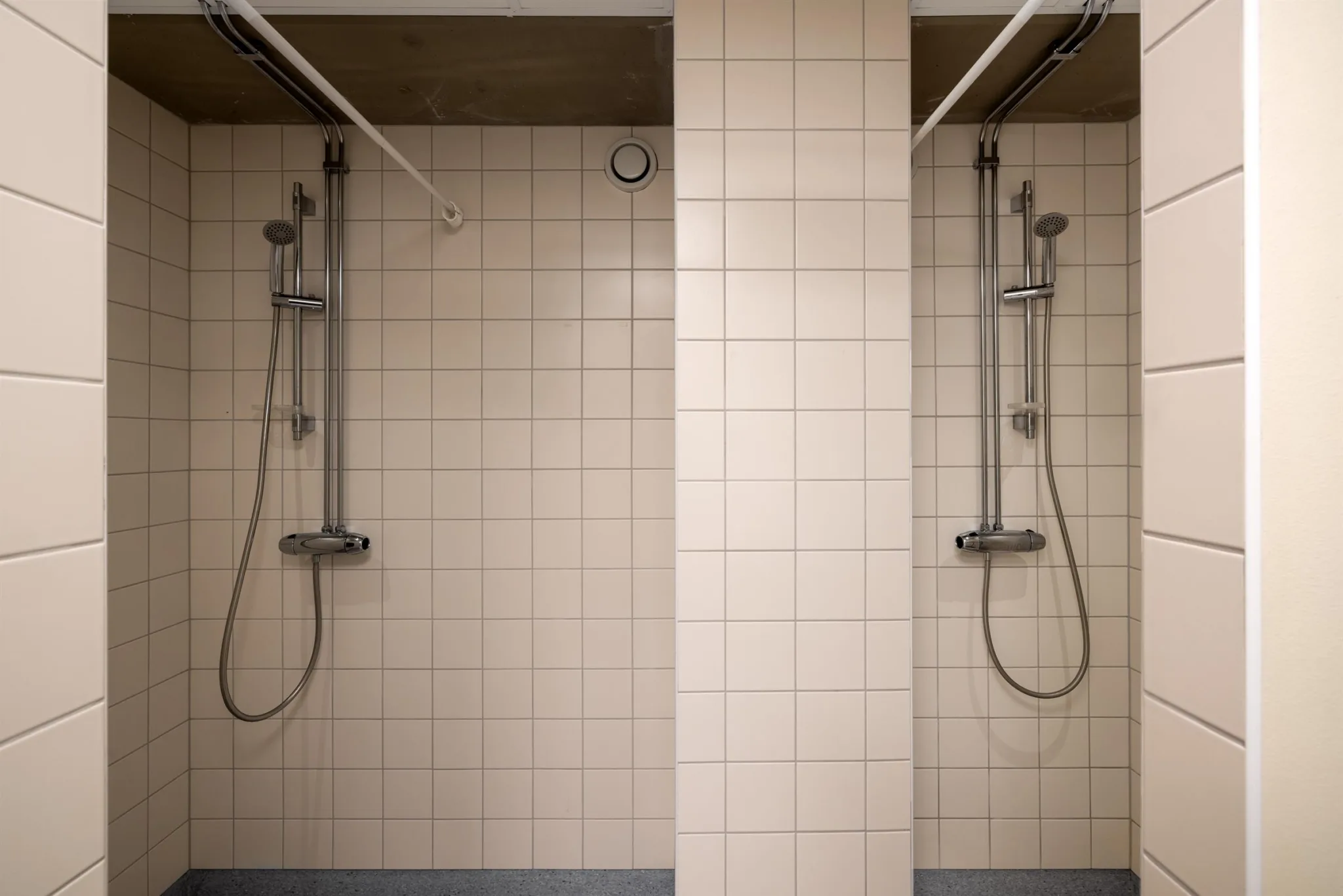 Två duschar med kaklade väggar, separerade av en kaklad pelare.