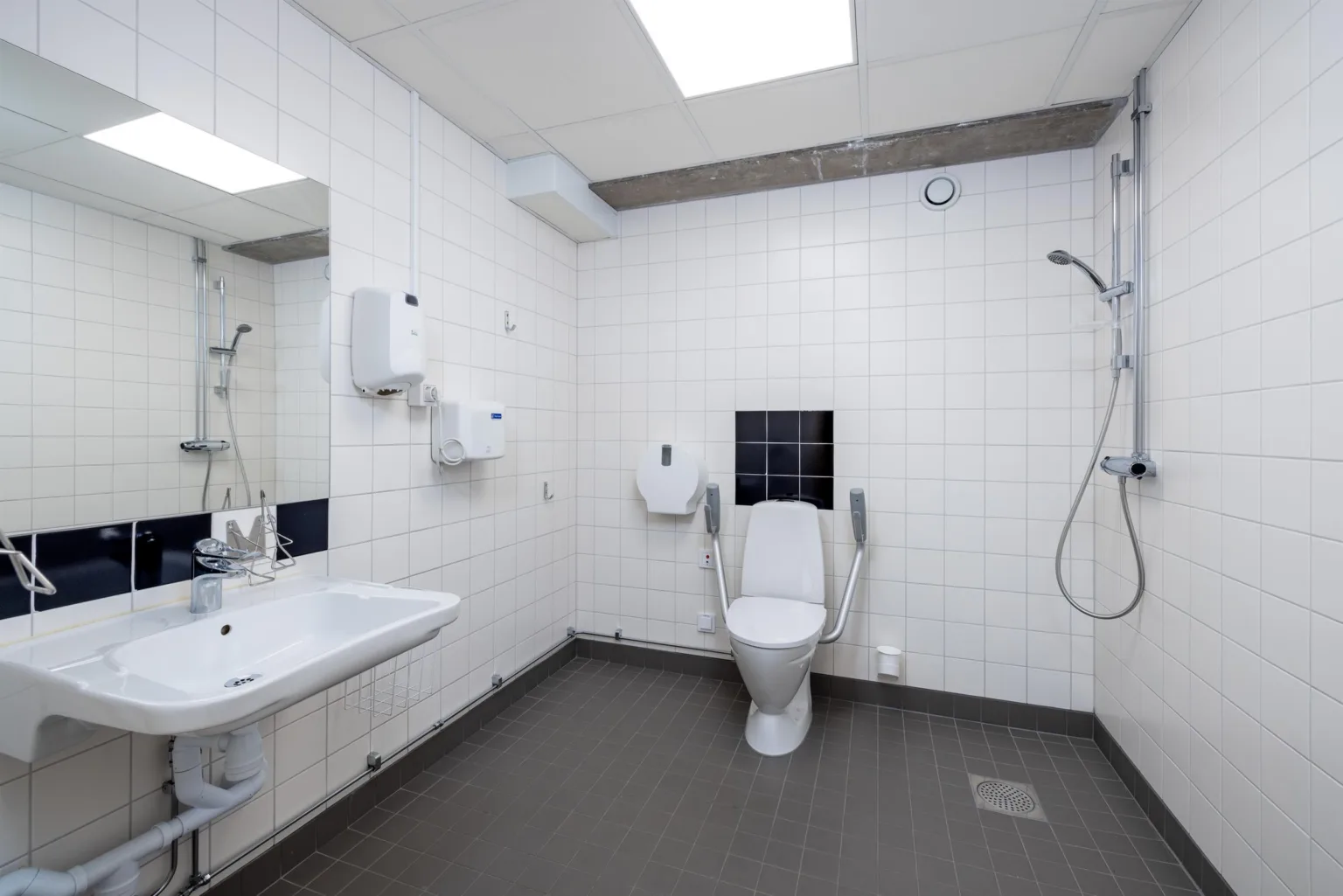 2. Ett badrum med vita kaklade väggar, toalett, dusch och handfat under en taklampa.