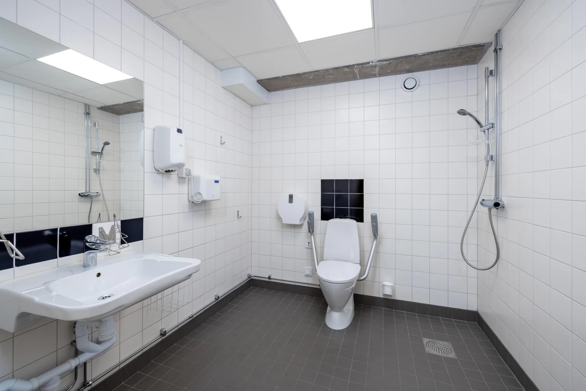 2. Ett badrum med vita kaklade väggar, toalett, dusch och handfat under en taklampa.