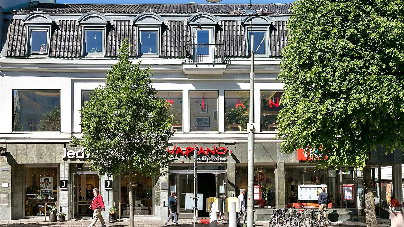 En byggnad med en butik på bottenvåningen, omgiven av träd och gångväg. Text på byggnaden: "KAPAND".