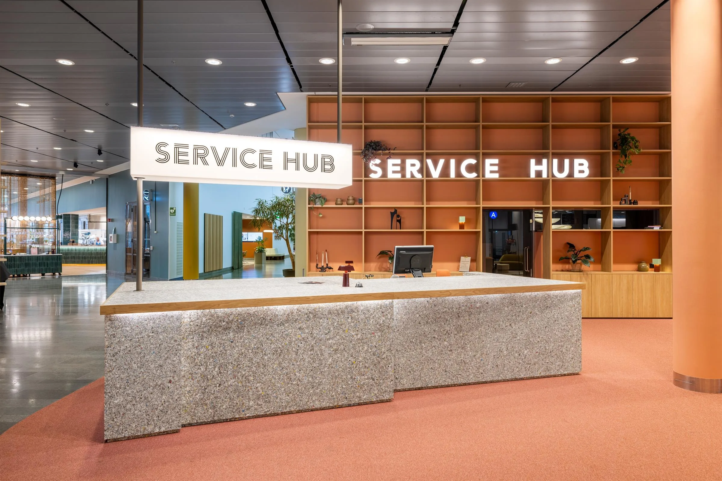 Reception med texten "Service Hub" på en skylt, omgiven av en modern miljö med träpaneler och en bänk.