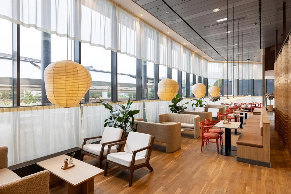 5. Ett ljust caféområde med stora fönster, sittmöbler, träbord och dekorativa lampskärmar.