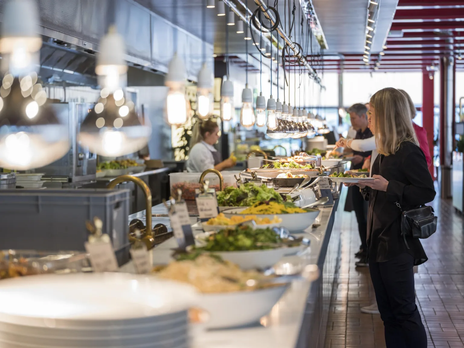 3. Buffé med salladsbord, flera personer fyller sina tallrikar i en ljus restaurangmiljö.