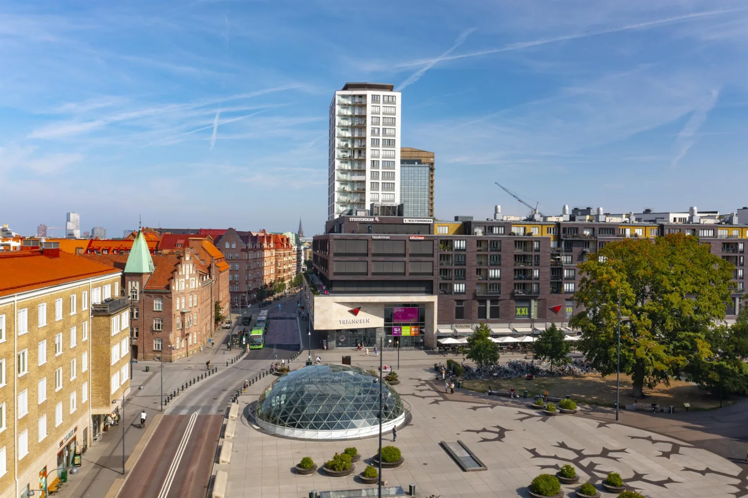 En stadsmiljö med moderna och äldre byggnader, en glasstruktur och spårvägar.